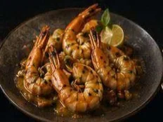King prawns cooked in garlic butter and cekuh, served on a dark plate